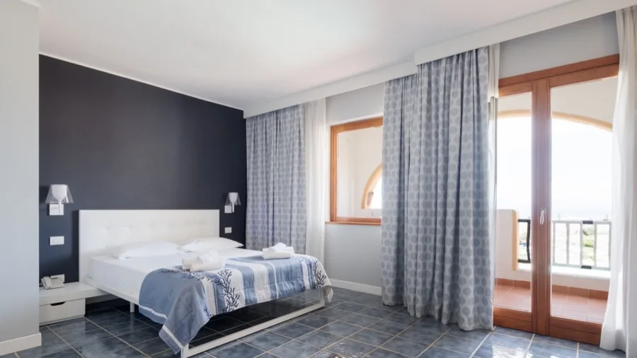 Camera da letto con letto matrimoniale, tende e balcone con vista. Parete blu e finestra a forma di finestra.