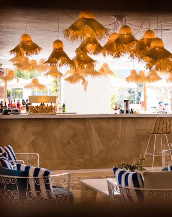 Luminari di paglia illuminate sopra un bar in un ambiente interno con sedie e tavoli.