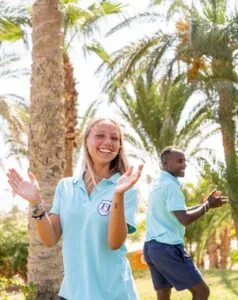 Due persone sorridenti in polo azzurra che applaudono all'aperto tra palme in un ambiente soleggiato.