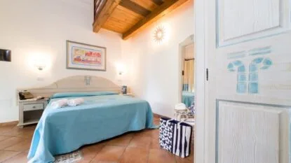 Camera da letto con letto matrimoniale, lenzuola azzurre, armadio in legno chiaro e decorazioni mediterranee.