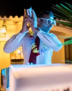 Uomo con occhiali da sole e collana di fiori, che sceglie uno shaker per il cocktail durante una festa serale.