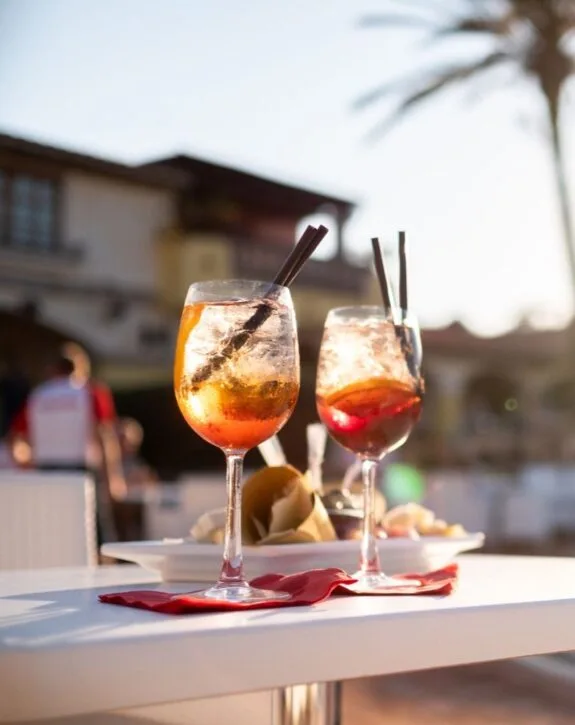 Due bicchieri di cocktail con ghiaccio e cannucce, su un tavolo all'aperto al tramonto.