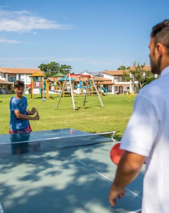 Ragazzo gioca a ping pong con un adulto in un parco giochi all'aperto.
