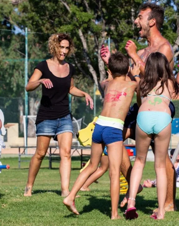 Famiglia che gioca e si diverte con vernici colorate all'aperto, sorridendo e creando ricordi felici.