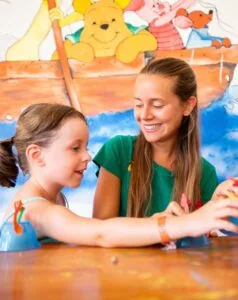 Bambina e ragazza sorridenti giocano insieme a un tavolo con un murale di Winnie the Pooh sullo sfondo.