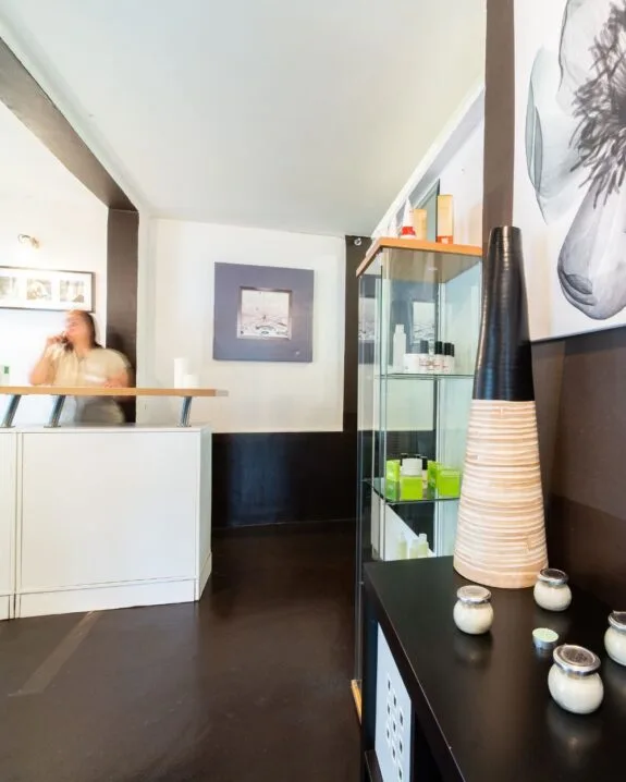 Interno di un centro benessere con un bancone, una vetrina di prodotti e decorazioni minimaliste. Una persona è in movimento.