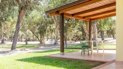 Veranda con sedia e tavolo verdi, circondata da un prato e alberi in un parco soleggiato.