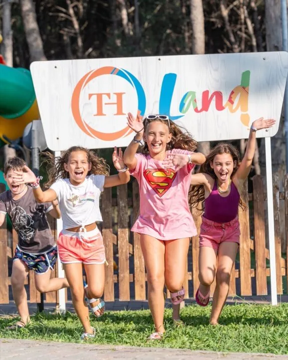 Quattro bambini felici che corrono verso la fotocamera davanti a un cartello colorato con la scritta "Land".