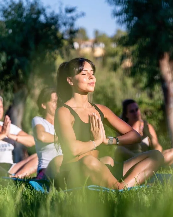 Donna che pratica yoga seduta a gambe incrociate con le mani in preghiera in un parco soleggiato.