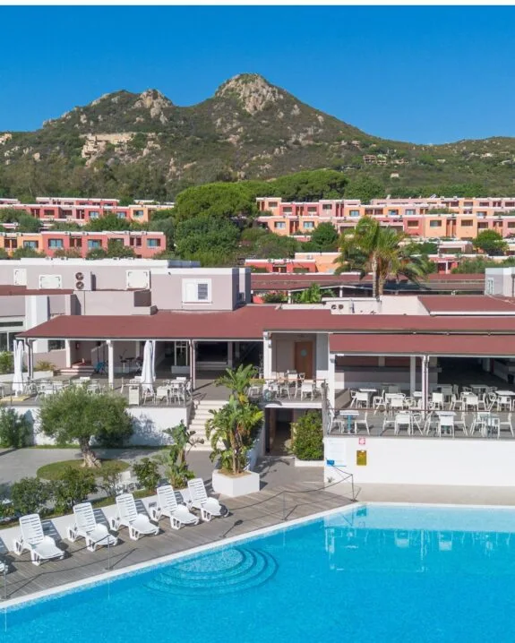 Vista panoramica di un resort con piscina, sdraio e colline sullo sfondo, in un ambiente soleggiato e accogliente.
