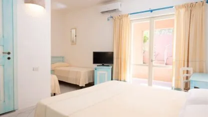 Camera luminosa con letto matrimoniale, letti singoli, TV, aria condizionata e porta finestra con tende chiare.