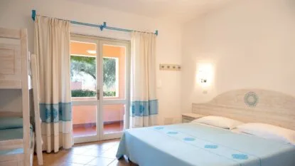 Camera da letto luminosa con letto matrimoniale, letto a castello in legno chiaro e porta finestra con tende crema e blu.
