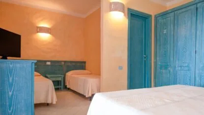 Camera con pareti arancioni, mobili in legno turchese, due letti singoli e un letto matrimoniale.