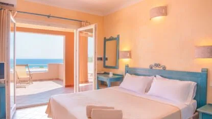 Camera matrimoniale luminosa con letto, mobili turchesi, balcone e vista mare sullo sfondo.