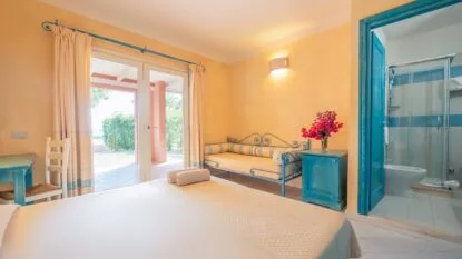 Camera luminosa con letto, divano in ferro battuto azzurro, comodino con fiori e bagno con doccia.
