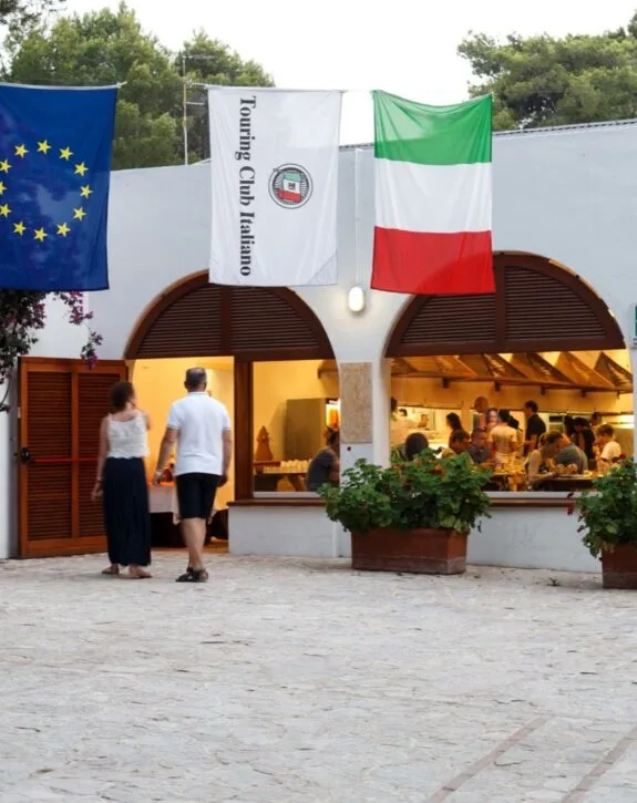 Persone che entrano in un ristorante con bandiere di Europa, Italia e Touring Club Italiano sopra l'ingresso.