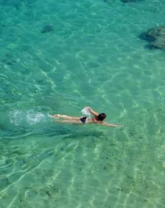 Ragazza che nuota in acque chiare e turchesi, vista dall'alto.