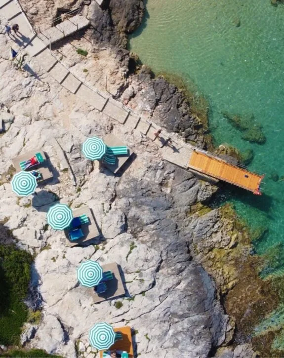 Veduta aerea di lettini con ombrelloni sulla scogliera vicino al mare.