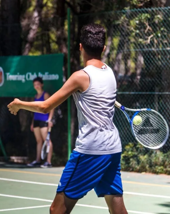 Giocatore di tennis pronto a colpire una palla sulla rete, con avversaria in background, campo e rete.