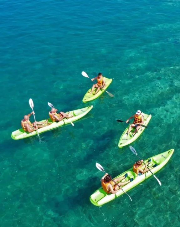 Cinque persone in kayak gialli sulla spiaggia, che navigano in acque cristalline.