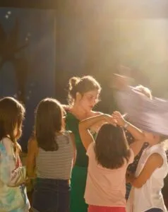 Donna con capelli raccolti circondata da bambini, luce calda e sfondo sfocato.