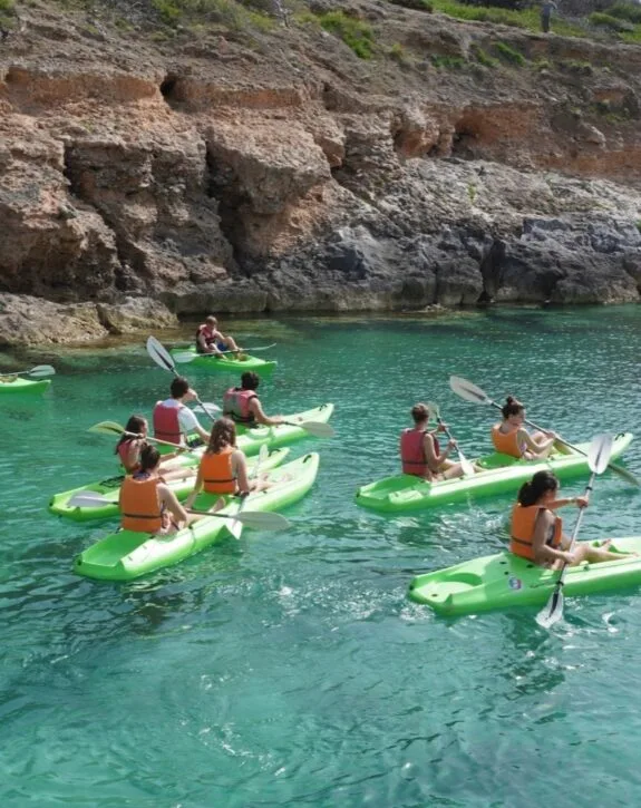 Gruppo di persone in kayak verdi in acque cristalline vicino a una scogliera rocciosa.