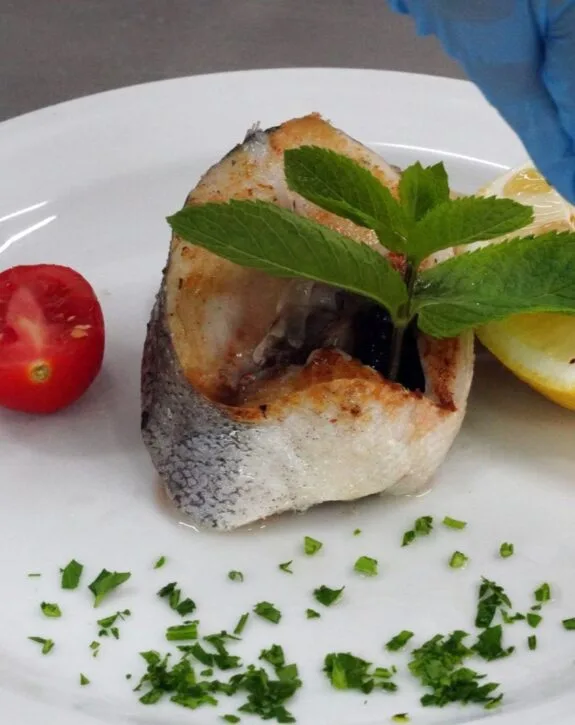 Piatto di pesce grigliato con menta fresca, pomodoro e limone, decorato con prezzemolo tritato.