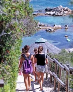 Gruppo di ragazze che passeggiano su un sentiero costiero, con vista sul mare blu e rocce sullo sfondo.