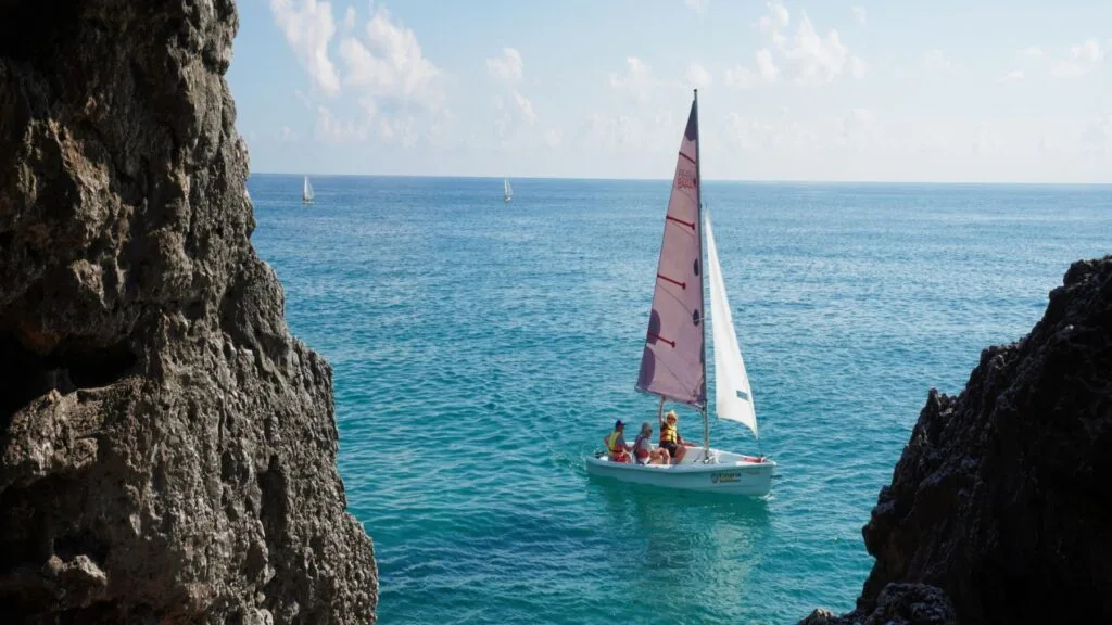 Vela a vela tra le scogliere, con il mare blu e il cielo sereno sullo sfondo.