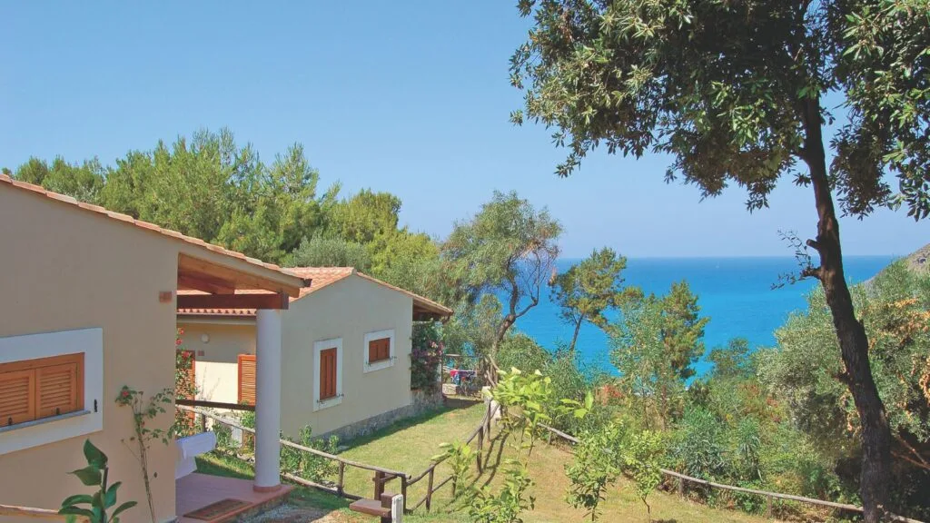 Case sul mare circondate da alberi e vegetazione, con vista sull'oceano azzurro.