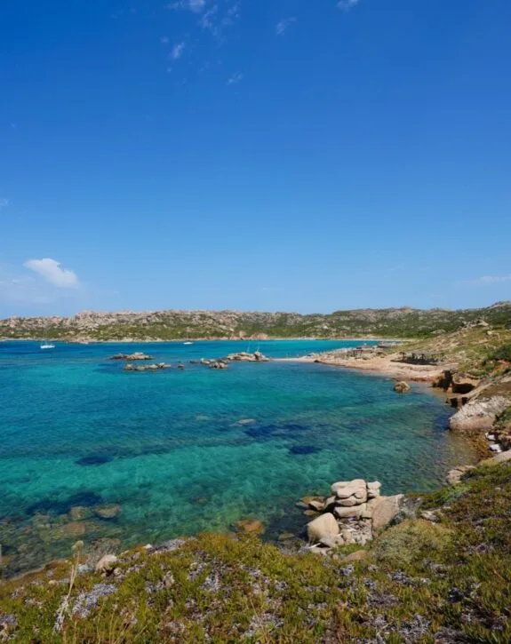 Scorcio di una baia con acque turchesi, scogli e vegetazione, sotto un cielo sereno.