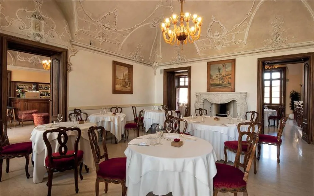 Sala ristorante elegante con soffitto affrescato, camino in marmo e tavoli rotondi apparecchiati
