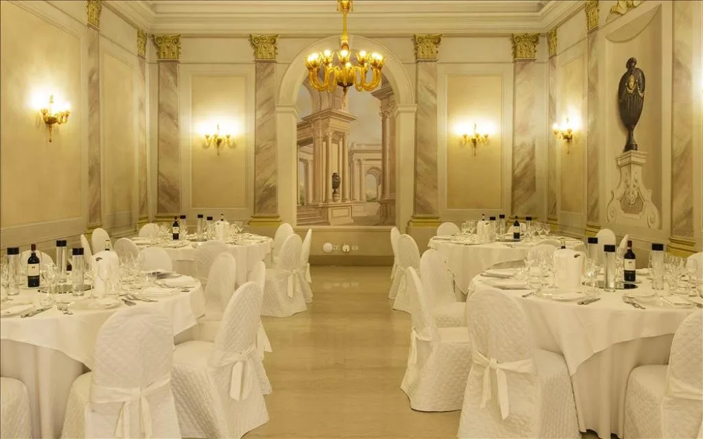 Sala banchetti con pareti in finto marmo, affresco prospettico e tavoli rotondi allestiti per eventi