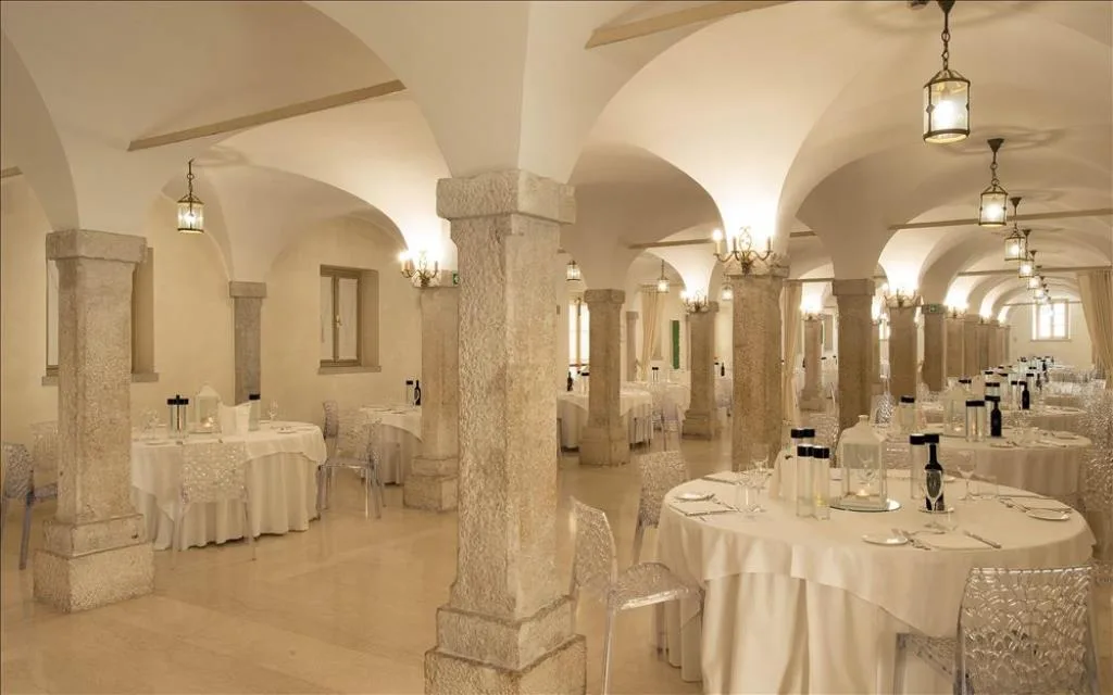 Sala ristorante con volte a crociera e colonne in pietra, tavoli rotondi apparecchiati in bianco