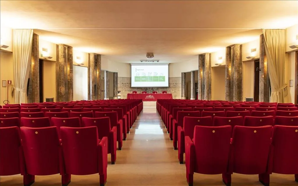 Sala conferenze in stile auditorium con poltrone rosse e schermo per proiezioni