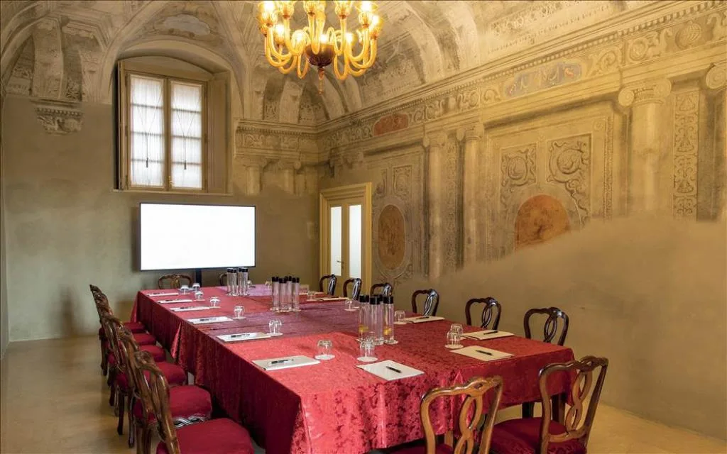 Sala meeting con pareti affrescate, tavolo unico e schermo, allestimento riservato