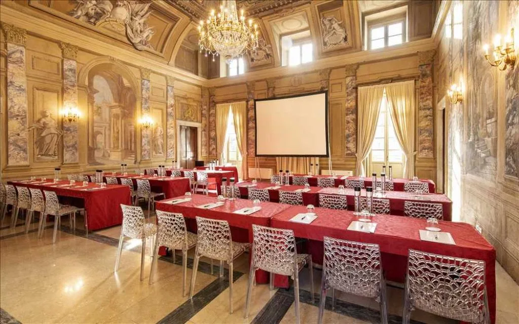 Elegante sala meeting con affreschi, lampadario di cristallo e tavoli disposti a platea