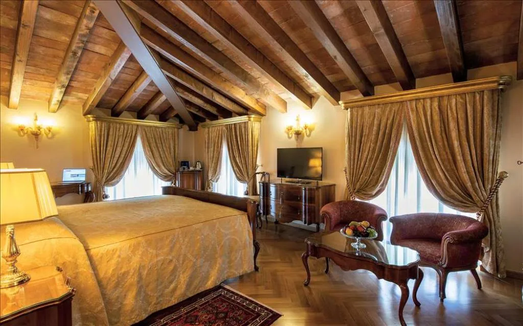 Suite mansardata con soffitto in travi di legno, tende dorate e zona salotto