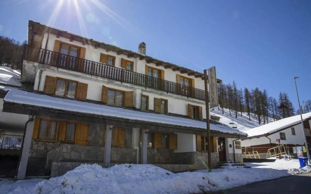 Facciata del residence di montagna con balconi in legno e neve, illuminata dal sole