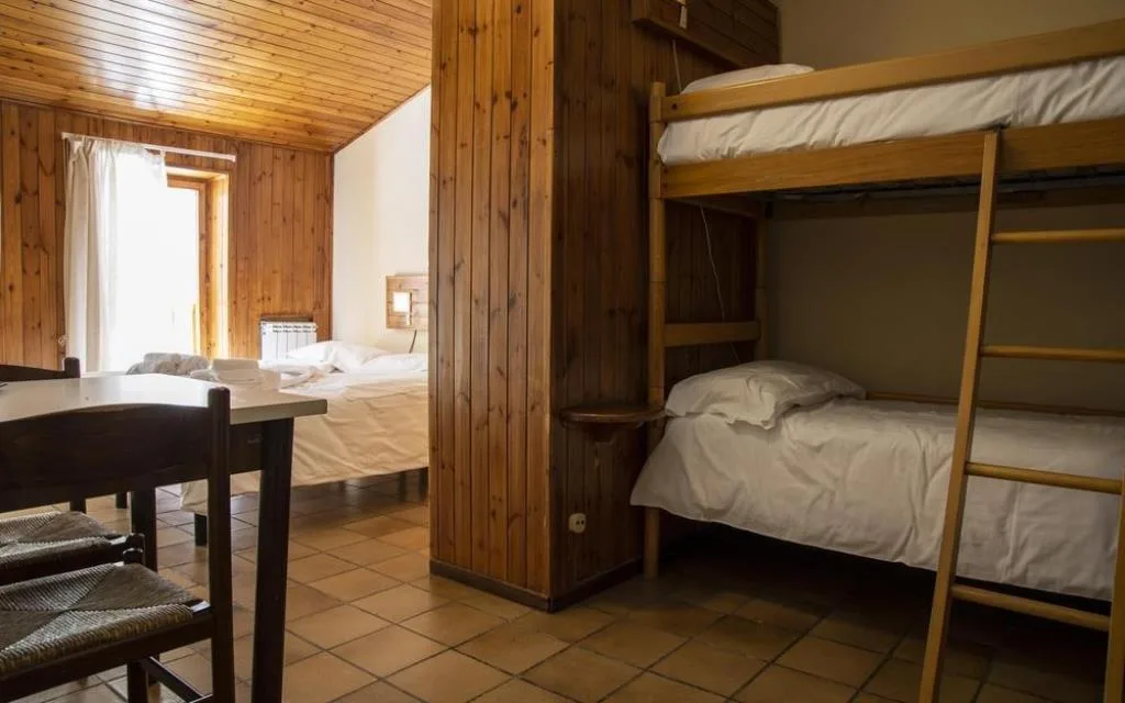 Camera rivestita in legno con letto matrimoniale, letto a castello e tavolo da pranzo
