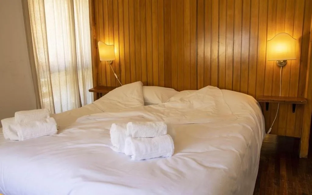 Camera con letto matrimoniale, testiera in legno e lampade da parete accese