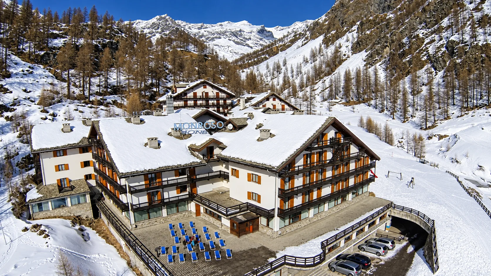 Vista dall'alto dell'hotel in stile alpino con tetti innevati e terrazza con lettini blu