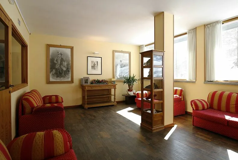 Area salotto dell'hotel con poltrone rosse a righe, pavimento in legno e stampe alle pareti