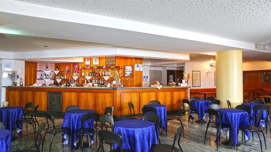 Bar interno dell'hotel con bancone in legno e tavolini rotondi con tovaglie blu