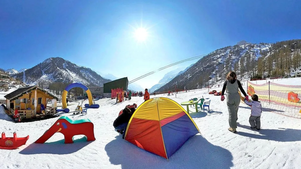 Area giochi per bambini sulla neve con tenda colorata, scivoli e giochi gonfiabili sotto il sole