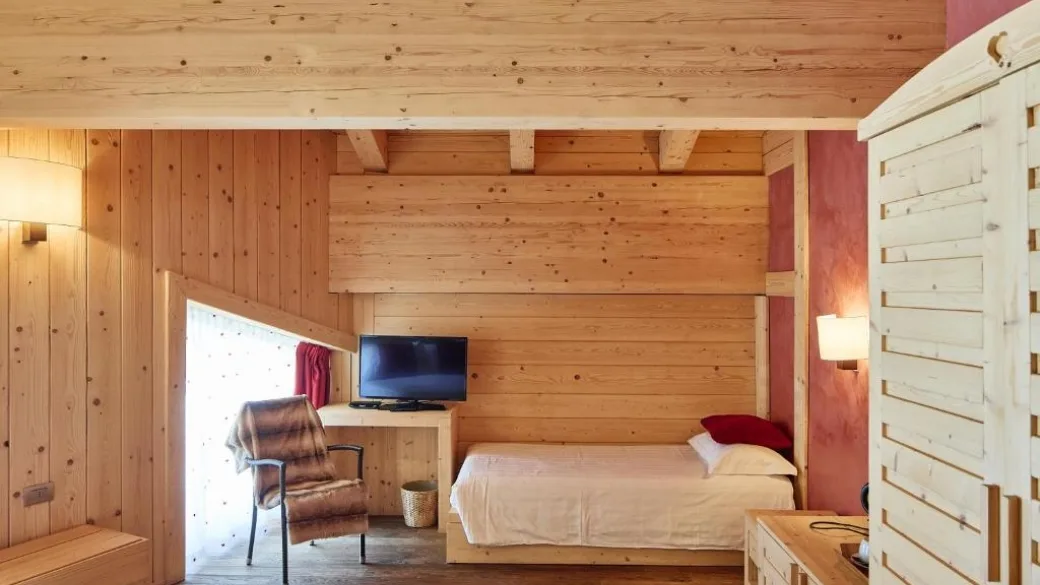 Camera con letto singolo, pareti in legno e tonalità rosse e TV
