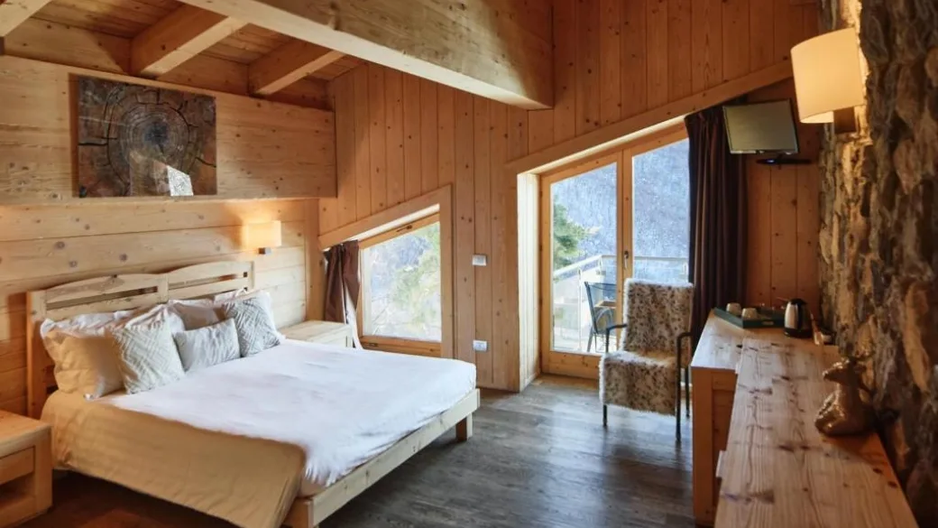 Camera in legno con letto matrimoniale, poltrona e grandi finestre panoramiche