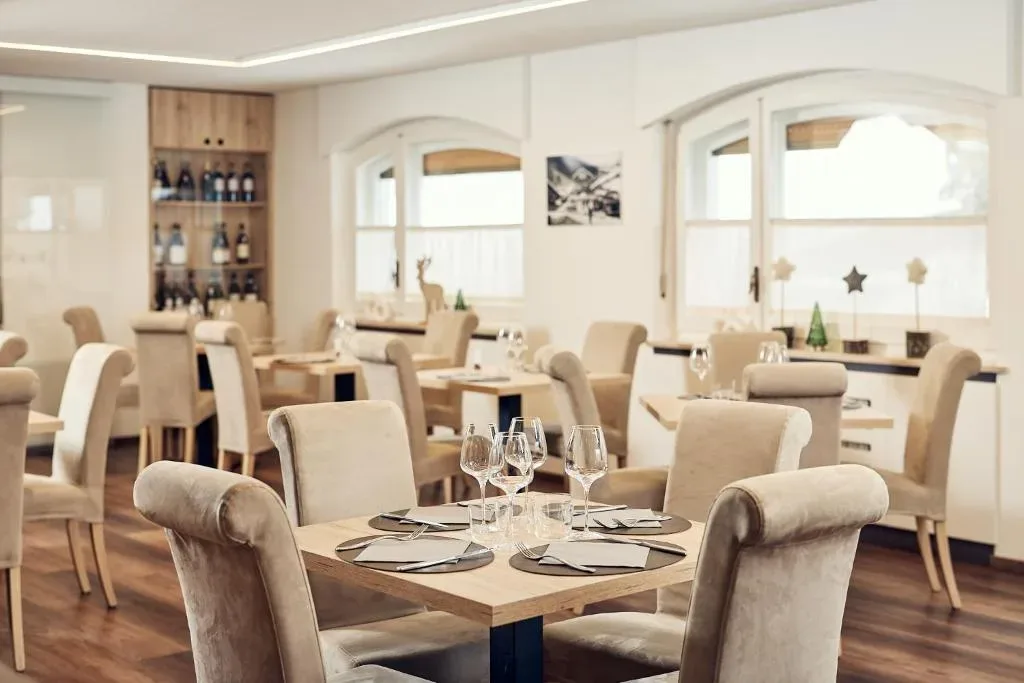 Sala ristorante elegante con tavoli apparecchiati e sedie beige imbottite
