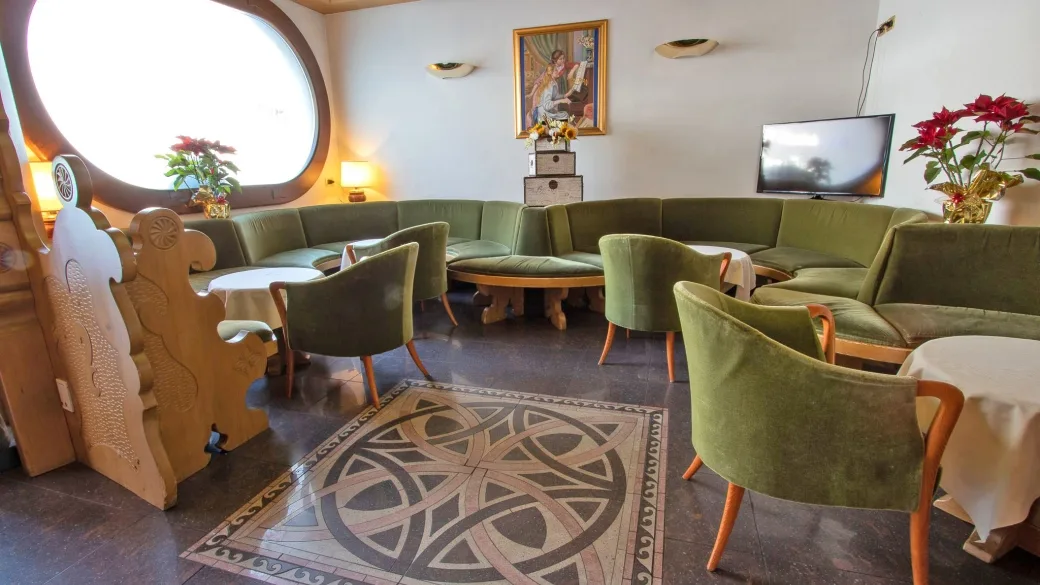 Salotto dell'hotel con divani verdi, finestra rotonda e mosaico sul pavimento