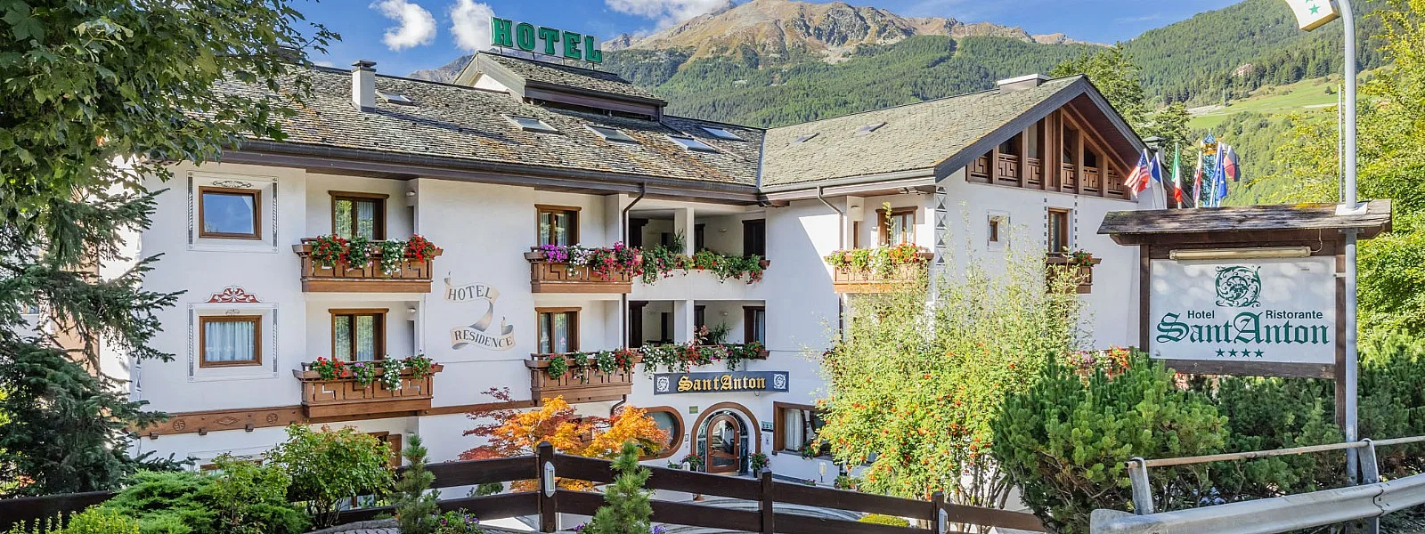 Facciata dell'Hotel Sant'Anton in estate con balconi fioriti e montagne verdi
